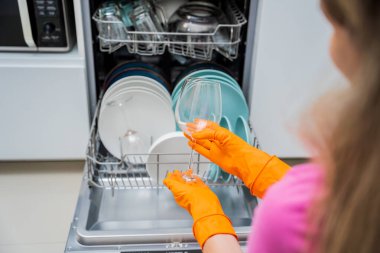 Genç kadın bulaşık makinesinden bulaşıkları çıkarıyor..