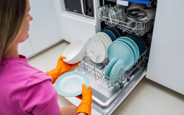 Genç kadın bulaşık makinesinden bulaşıkları çıkarıyor..