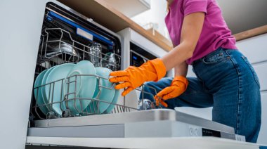 Genç kadın bulaşık makinesinden bulaşıkları çıkarıyor..