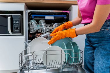 Genç kadın bulaşık makinesinden bulaşıkları çıkarıyor..