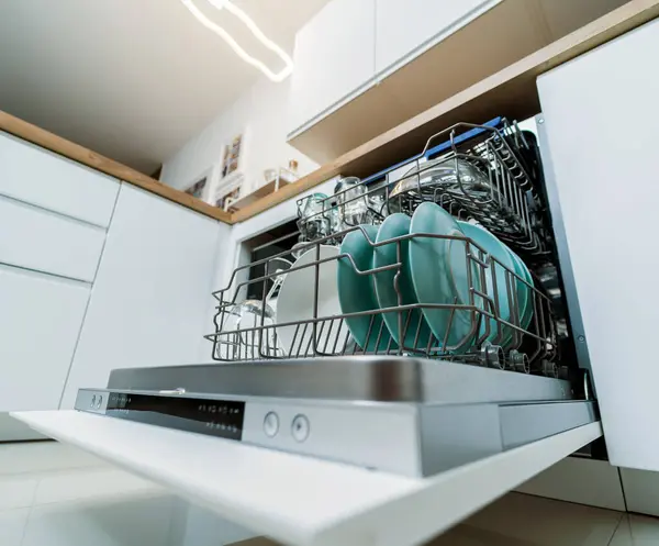 The white kitchen and opened dishwasher with clean dishes.