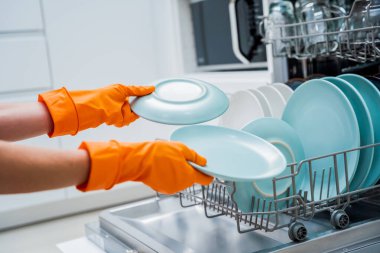 Genç kadın bulaşık makinesinden bulaşıkları çıkarıyor..