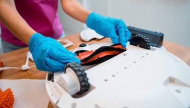 Genç bir kadın temizlik yaptıktan sonra robot elektrik süpürgesini pislikten temizliyor.