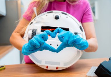 Genç bir kadın temizlik yaptıktan sonra robot elektrik süpürgesini pislikten temizliyor.