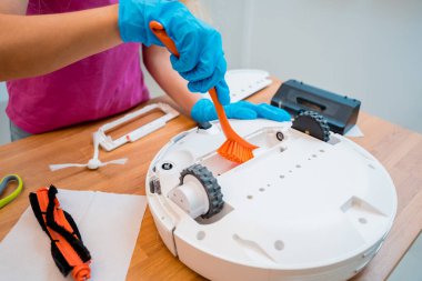 Genç bir kadın temizlik yaptıktan sonra robot elektrik süpürgesini pislikten temizliyor.