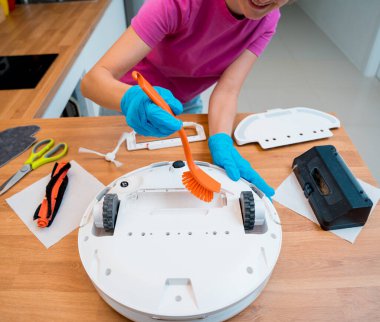 Genç bir kadın temizlik yaptıktan sonra robot elektrik süpürgesini pislikten temizliyor.