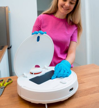 Genç bir kadın temizlik yaptıktan sonra robot elektrik süpürgesini pislikten temizliyor.