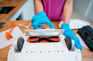 Genç bir kadın temizlik yaptıktan sonra robot elektrik süpürgesini pislikten temizliyor.