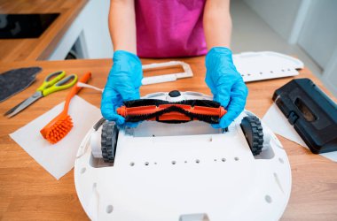 Genç bir kadın temizlik yaptıktan sonra robot elektrik süpürgesini pislikten temizliyor.