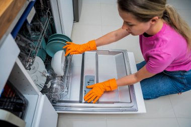 Genç kadın bulaşık makinesinden bulaşıkları çıkarıyor..