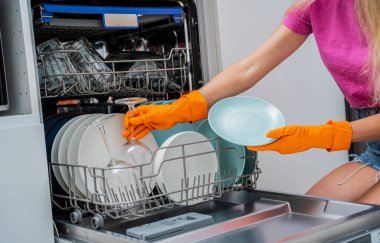 Genç kadın bulaşık makinesinden bulaşıkları çıkarıyor..