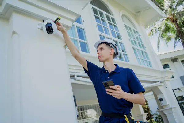 A technician installs a CCTV camera on the facade of a residential building