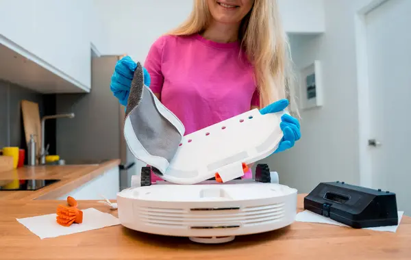 A young woman cleans a robot vacuum cleaner from dirt after cleaning