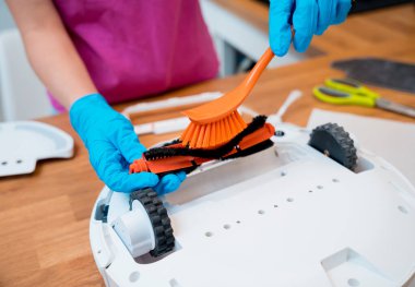 Genç bir kadın temizlik yaptıktan sonra robot elektrik süpürgesini pislikten temizliyor.