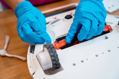Genç bir kadın temizlik yaptıktan sonra robot elektrik süpürgesini pislikten temizliyor.