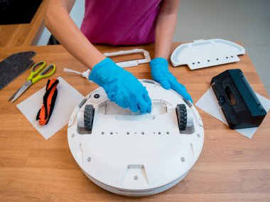 Genç bir kadın temizlik yaptıktan sonra robot elektrik süpürgesini pislikten temizliyor.