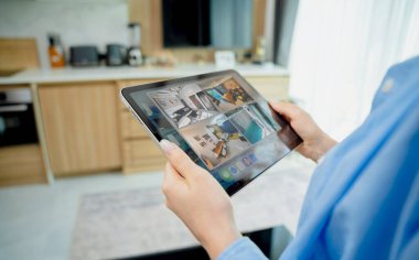 Tablet bilgisayardaki güvenlik kameralarına bakan genç bir kadın..