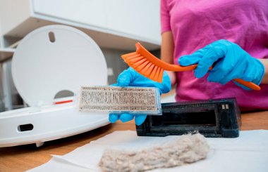 Genç bir kadın temizlik yaptıktan sonra robot elektrik süpürgesini pislikten temizliyor.