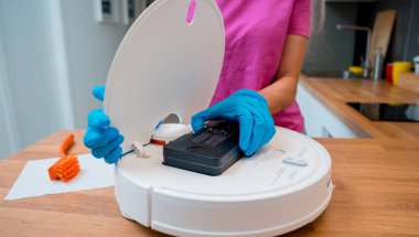 Genç bir kadın temizlik yaptıktan sonra robot elektrik süpürgesini pislikten temizliyor.