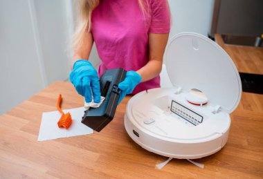 Genç bir kadın temizlik yaptıktan sonra robot elektrik süpürgesini pislikten temizliyor.