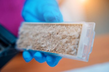 Genç bir kadın temizlik yaptıktan sonra robot elektrik süpürgesini pislikten temizliyor.