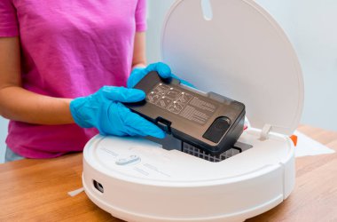 Genç bir kadın temizlik yaptıktan sonra robot elektrik süpürgesini pislikten temizliyor.