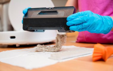 Genç bir kadın temizlik yaptıktan sonra robot elektrik süpürgesini pislikten temizliyor.