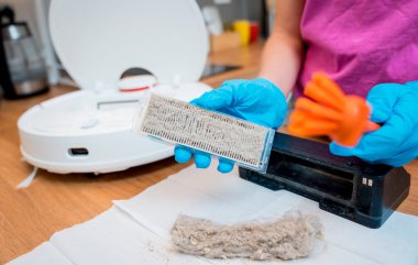 Genç bir kadın temizlik yaptıktan sonra robot elektrik süpürgesini pislikten temizliyor.