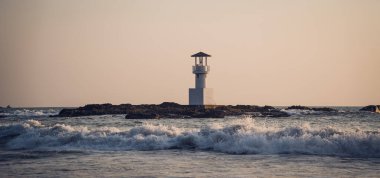 Deniz feneri suyla çevrili ve bulutlu gün batımı gökyüzü.
