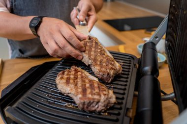 Şef mutfakta ev yapımı elektrikli ızgarada biftek hazırlıyor..