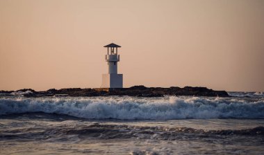 Deniz feneri suyla çevrili ve bulutlu gün batımı gökyüzü.