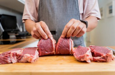 Şef mutfakta, ev yapımı elektrikli ızgarada biftekler için çiğ biftek hazırlıyor..