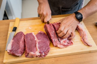 Şef mutfakta, ev yapımı elektrikli ızgarada biftekler için çiğ biftek hazırlıyor..