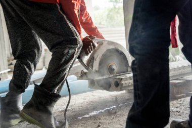 Büyük bir beton parçası kesmek için dairesel testere kullanan bir inşaatçı..