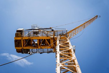 Büyük sarı bir vinç parlak mavi bir gökyüzüne karşı duruyor..