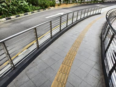 Korkuluklu kavisli yol ve yol boyunca kör insanlar için sarı çizgi.