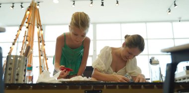 Genç anne ve kızı cadılar bayramı kurabiyelerini geniş bir modern atölyede boyuyorlar.