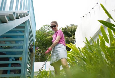 Genç bir kadın güzel bahçesini süslüyor canlı yeşilliğini ve açık hava aktivitelerine olan aşkını sergiliyor.