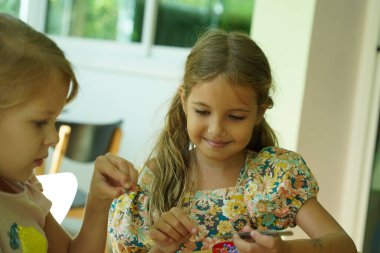 Sanat öğretmeni atölyede iki kıza termo mozaik montajı öğretiyor. 