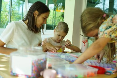 Sanat öğretmeni atölyede iki kıza termo mozaik montajı öğretiyor. 