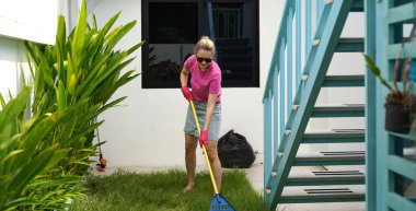 Evinin arka bahçesindeki çimenleri tırmıklayan genç bir kadın. 