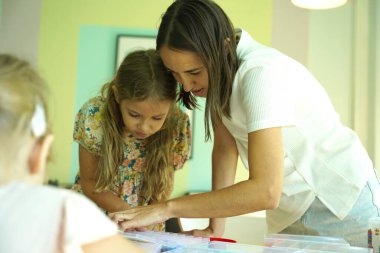 Sanat öğretmeni atölyede iki kıza termo mozaik montajı öğretiyor. 