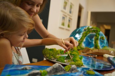 Genç bir anne ve kızı birlikte canlı doğal manzaralar yaratıyor. 