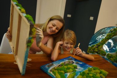 Genç bir anne ve kızı birlikte canlı doğal manzaralar yaratıyor. 