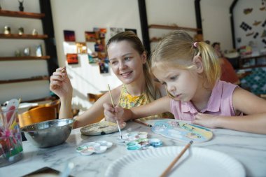 Genç bir anne ve kızı evde sanatsal bir seansın keyfini çıkarıyorlar. Renkli sanatlarıyla meşgul ve bağ kuruyorlar.