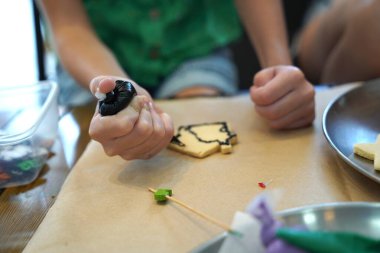 Genç anne ve kızı cadılar bayramı kurabiyelerini geniş bir modern atölyede boyuyorlar.