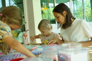 Sanat öğretmeni atölyede iki kıza termo mozaik montajı öğretiyor. 