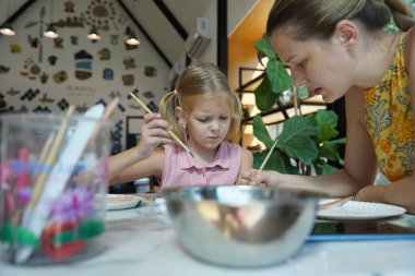 Genç bir anne ve kızı evde sanatsal bir seansın keyfini çıkarıyorlar. Renkli sanatlarıyla meşgul ve bağ kuruyorlar.