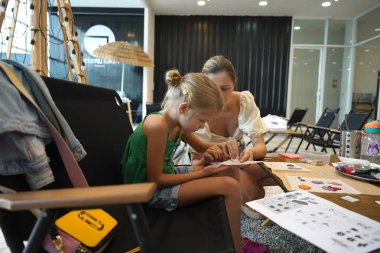 Genç anne ve kızı cadılar bayramı kurabiyelerini geniş bir modern atölyede boyuyorlar.