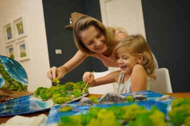 Genç bir anne ve kızı birlikte canlı doğal manzaralar yaratıyor. 